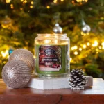 Brennende Christmas Tree Kerze neben Weihnachtskugeln und Tannenzapfen