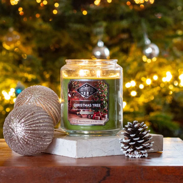 Brennende Christmas Tree Kerze neben Weihnachtskugeln und Tannenzapfen