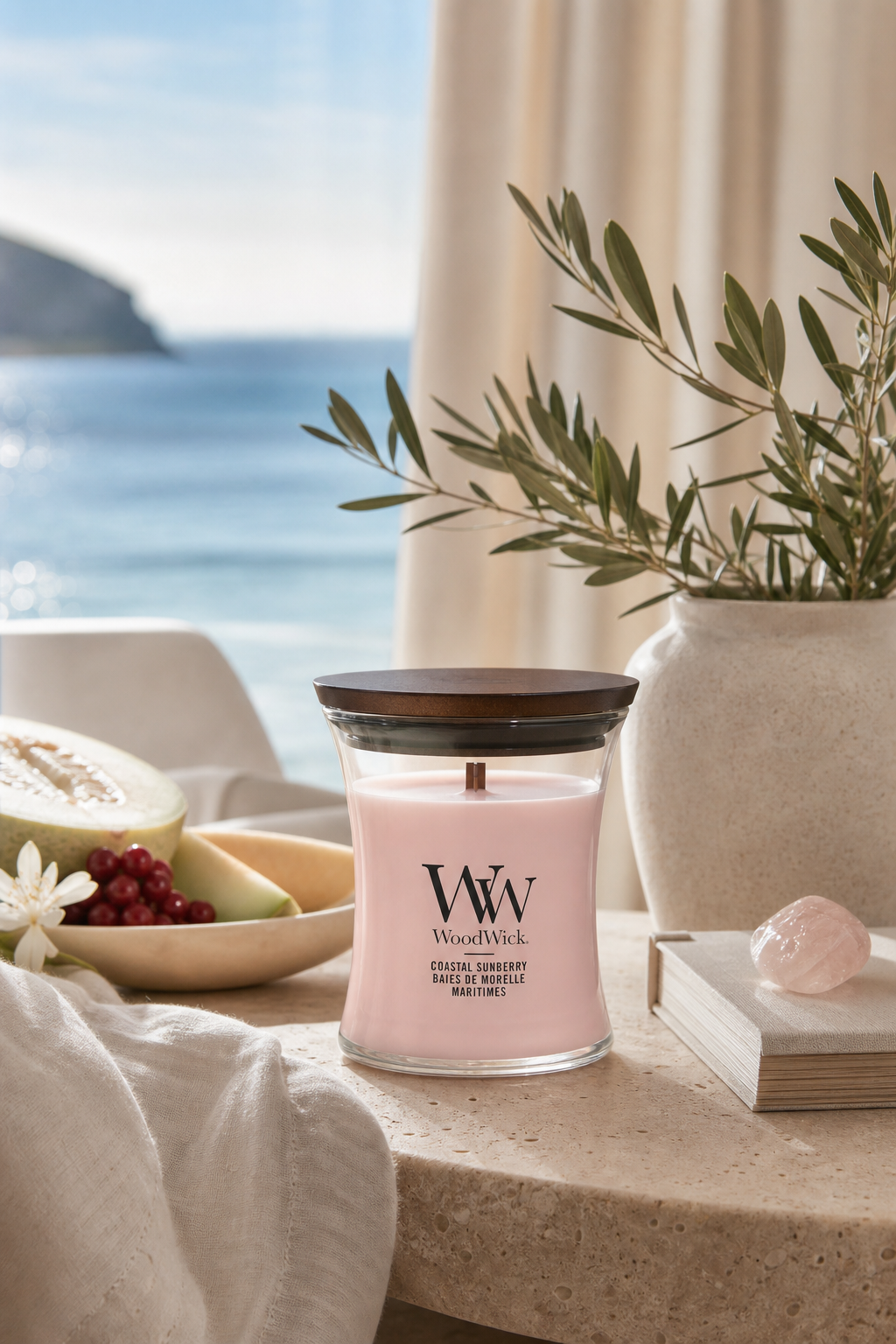 WoodWick Coastal Sunberry Kerze auf einem Tisch neben Büchern und Pflanze