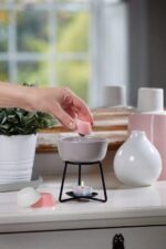Hand legt ein Wachsmelt in eine Duftlampe über einer brennenden Teelichtkerze
