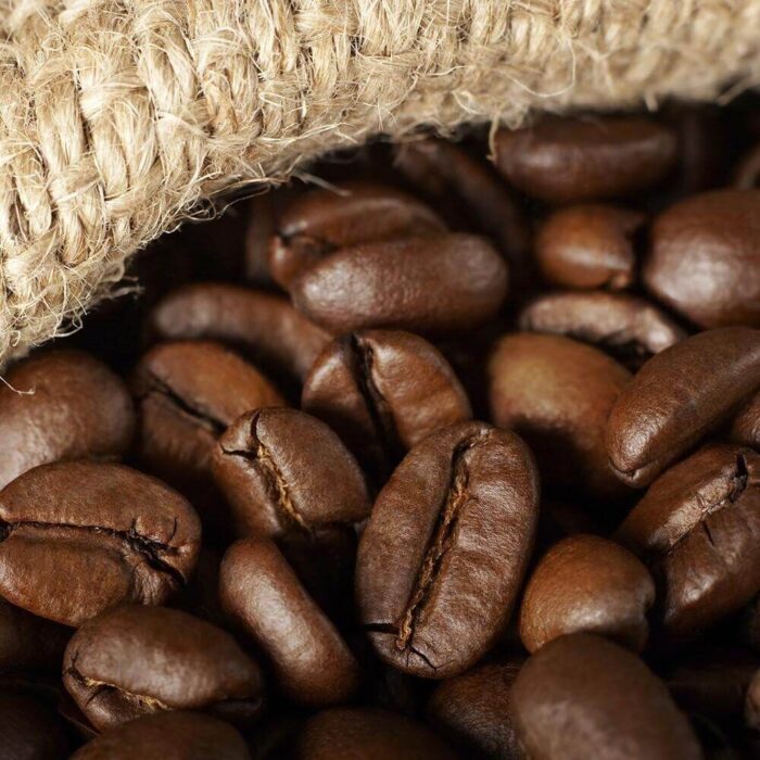 Village Candle Coffee Bean Kerze brennend auf einem Tisch neben Kaffeetasse