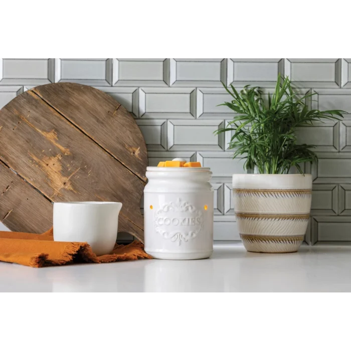 Weiße Cookie Jar Duftlampe mit Wachsstücken neben Pflanze und Keramikgefäß