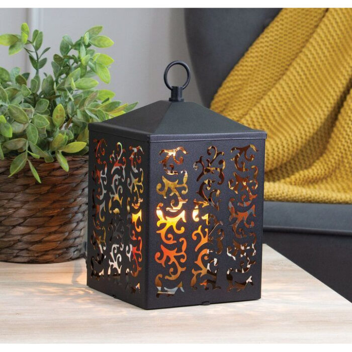 Schwarze Ornamentlaterne mit warmem Licht auf einem Tisch