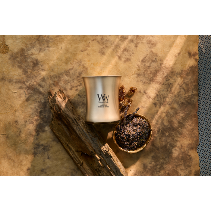 Brennende WoodWick Cypress Ore Kerze neben Holz und Schale mit getrockneten Pflanzen