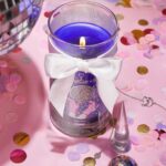 Brennende violette Kerze im Glas mit weißer Schleife und Armband daneben