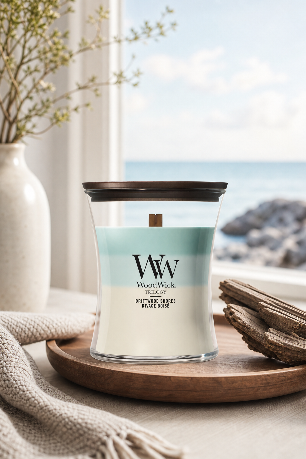 WoodWick Driftwood Shores Trilogy Kerze auf Holztablett vor Meerblick