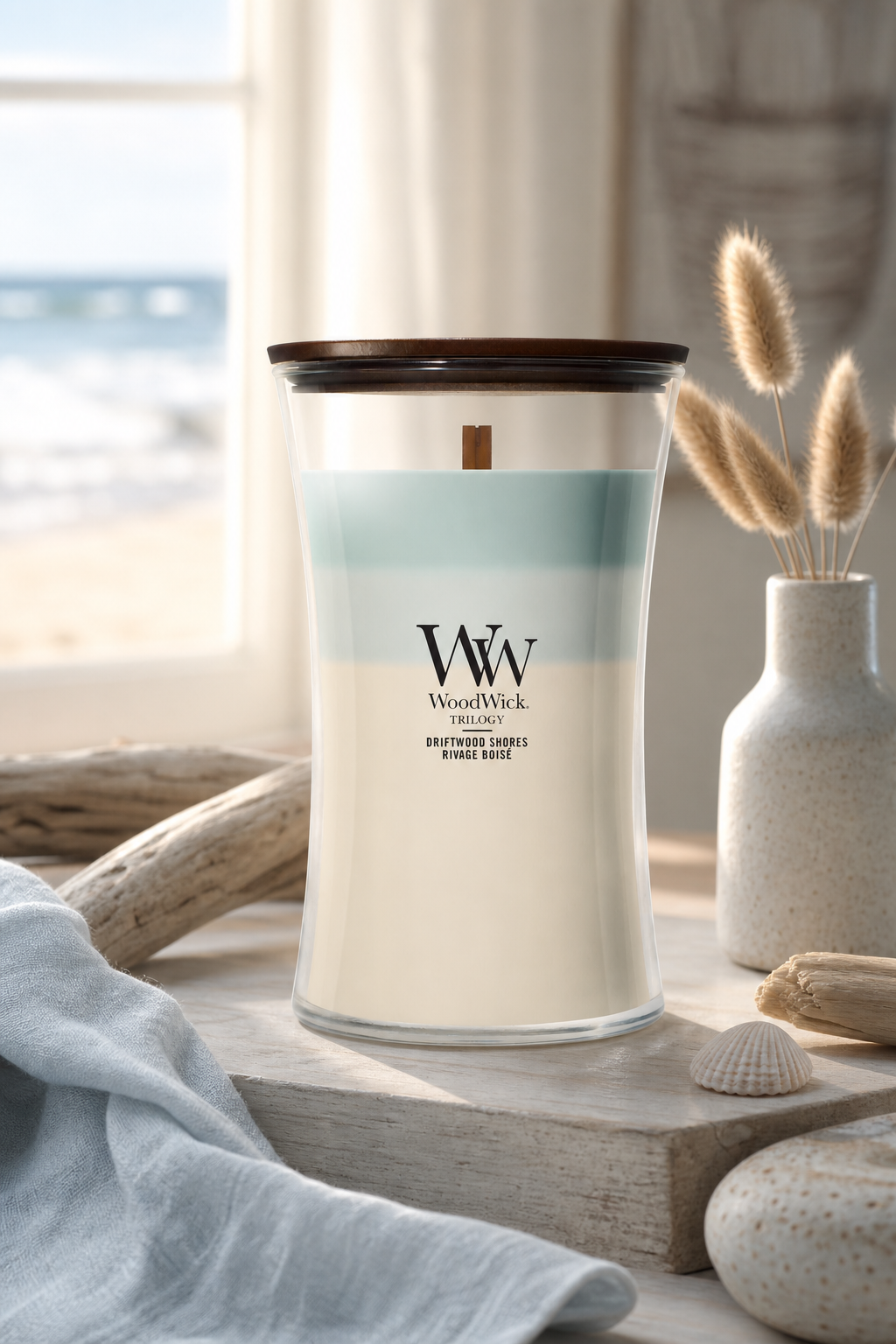 WoodWick Driftwood Shores Kerze auf Holztisch vor Fenster mit Strandblick