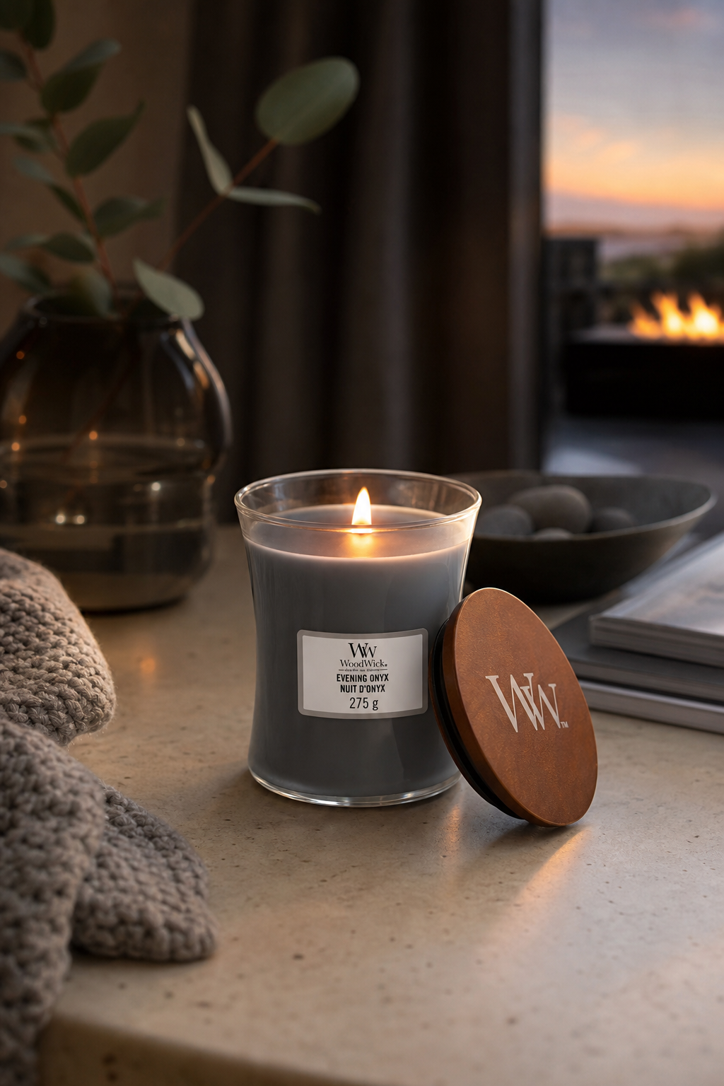 Brennende WoodWick Evening Onyx Kerze neben abgenommenem Holzdeckel auf Tisch