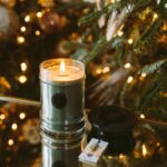 Brennende grüne Kerze neben schwarzem Deckel vor Weihnachtsbaum