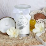 Fleur de Monoi Kerze neben Kokosnuss, Ölfläschchen und sichtbarem Schmuckarmband