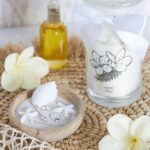 Fleur de Monoi Kerze neben Schale mit Schmuck, Muschel und weißen Blüten