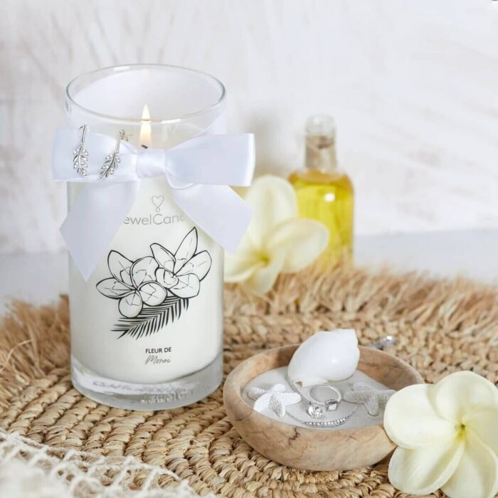 Brennende Fleur de Monoi Kerze mit Schleife neben Schmuckschale und Blüten