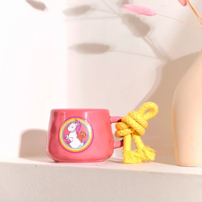 Pinke Kerzentasse mit Einhornmotiv und gelber Kordel auf einem Regal
