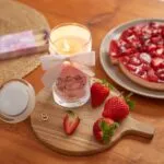 Brennende rosa Kerze mit weißer Schleife neben Erdbeeren und Kuchen