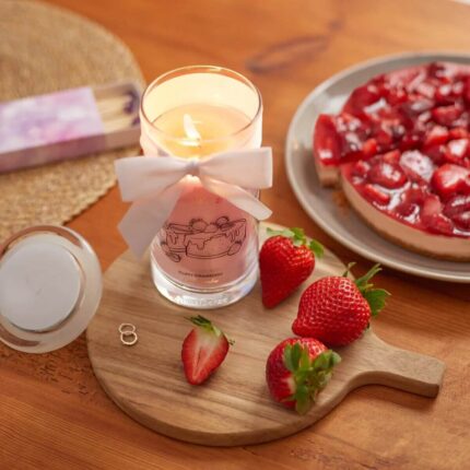 Brennende rosa Kerze mit weißer Schleife neben Erdbeeren und Kuchen