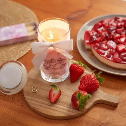 Brennende rosa Kerze mit weißer Schleife neben Erdbeeren und Kuchen