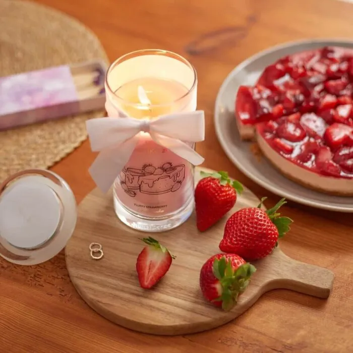 Brennende rosa Kerze mit weißer Schleife neben Erdbeeren und Kuchen