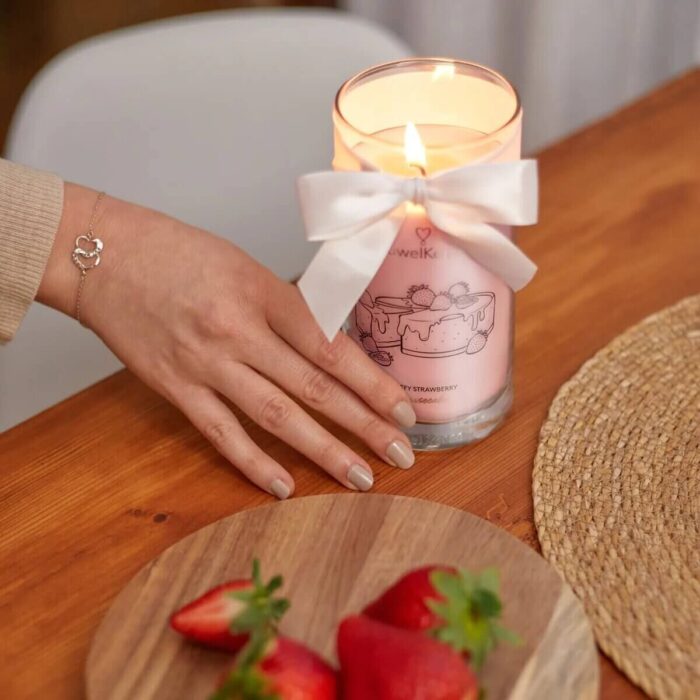 Brennende rosa Kerze mit Schleife neben Erdbeeren und einer Hand