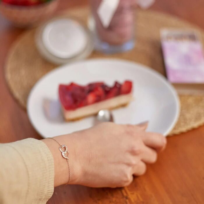 Hand mit Armband neben brennender rosa Kerze und Erdbeeren