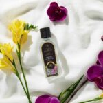Flasche Freesia & Orchid Lamp Fragrance liegt auf weißem Stoff mit Blüten