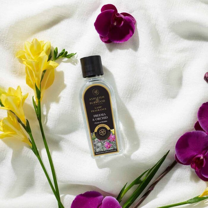 Flasche Freesia & Orchid Lamp Fragrance liegt auf weißem Stoff mit Blüten