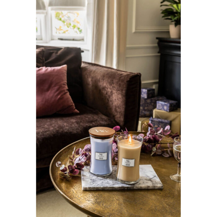 Brennende Gilded Sands Kerze neben einer violetten WoodWick Kerze auf Marmorsockel