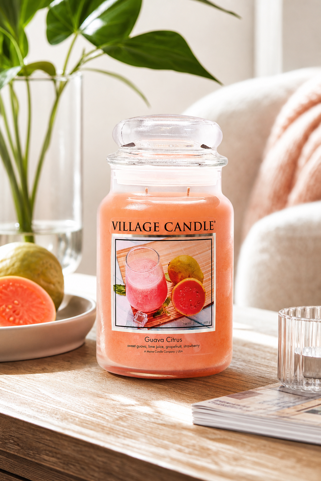 Village Candle Guava Citrus Kerze im Glas auf einem Tisch neben Pflanzen und Früchten