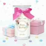 Happy-Birthday-Kerze mit Schleife neben mehreren hängenden Schmuckanhängern