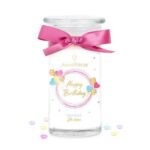 Happy-Birthday-Kerze mit rosa Schleife zwischen zwei dekorierten Geschenkboxen