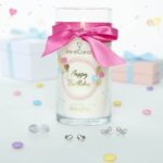 Happy-Birthday-Kerze mit rosa Schleife zwischen zwei Geschenkboxen