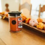 Harvest Pumpkin Kerze auf Holztisch neben verschiedenen Kürbissen