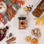Harvest Pumpkin Kerze zwischen Herbstdekor, Gewürzen, Gebäck und Kürbissen
