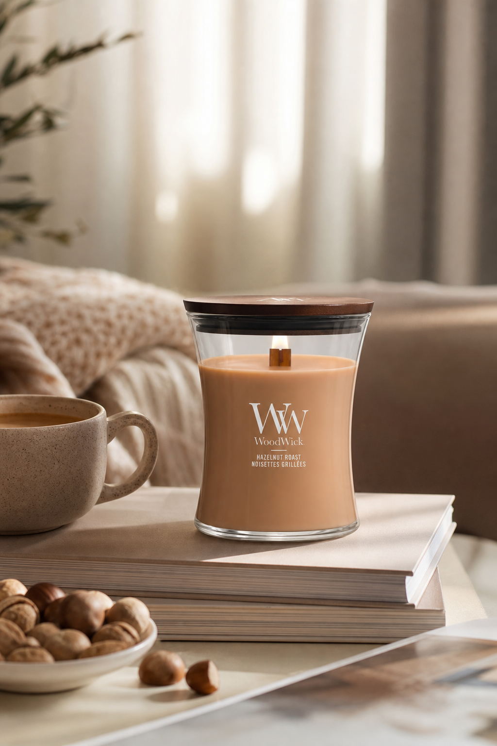 WoodWick Hazelnut Roast Kerze auf Büchern neben einer Tasse und Haselnüssen
