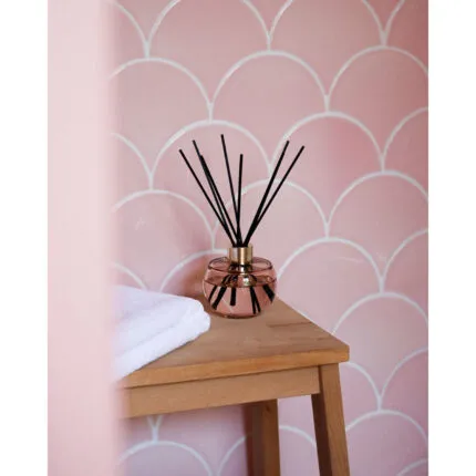 Raumduft-Diffuser mit schwarzen Stäbchen auf einem Beistelltisch vor rosafarbener Wand