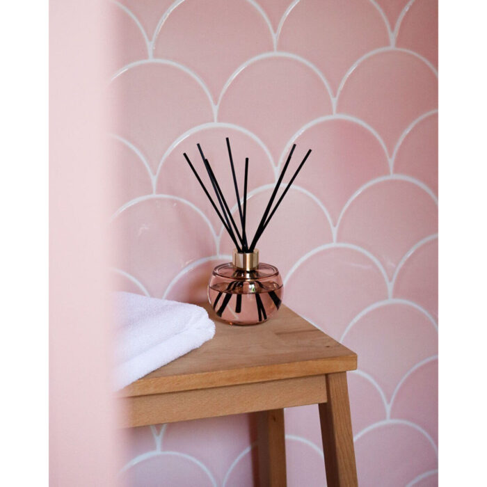 Raumduft-Diffuser mit schwarzen Stäbchen auf einem Beistelltisch vor rosafarbener Wand