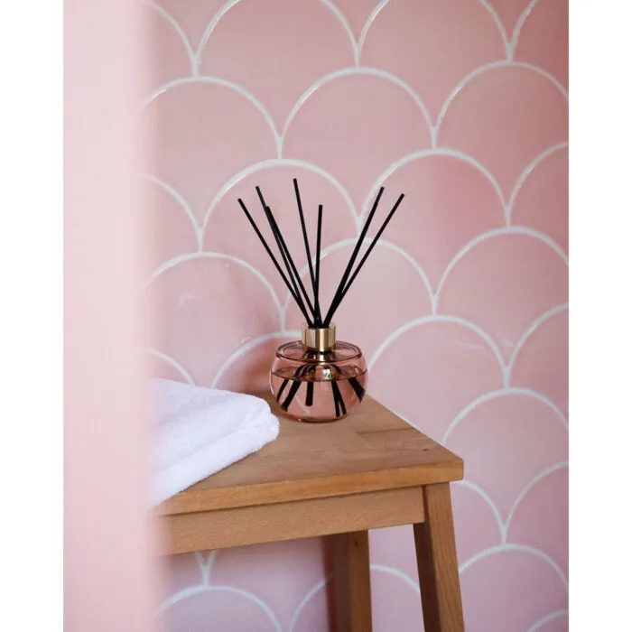 Raumduft-Diffuser mit schwarzen Stäbchen auf einem Beistelltisch vor rosafarbener Wand