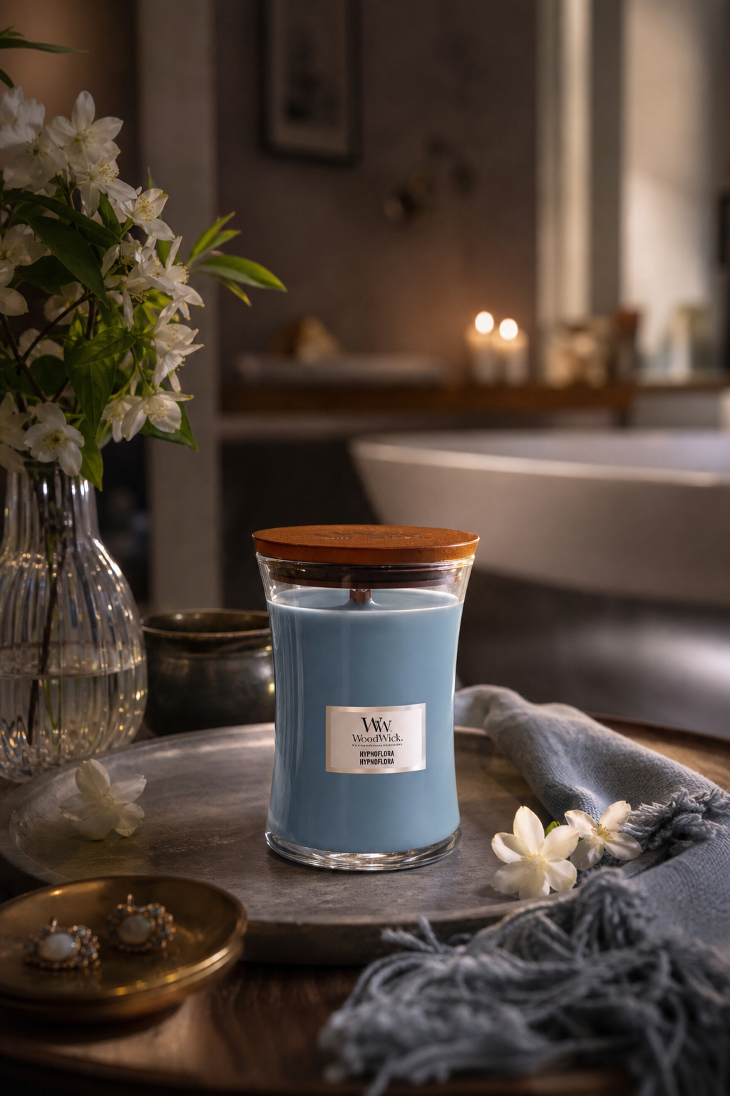 WoodWick Hypnoflora Kerze mit Holzdeckel auf einem Tablett neben Blumen und Textilien
