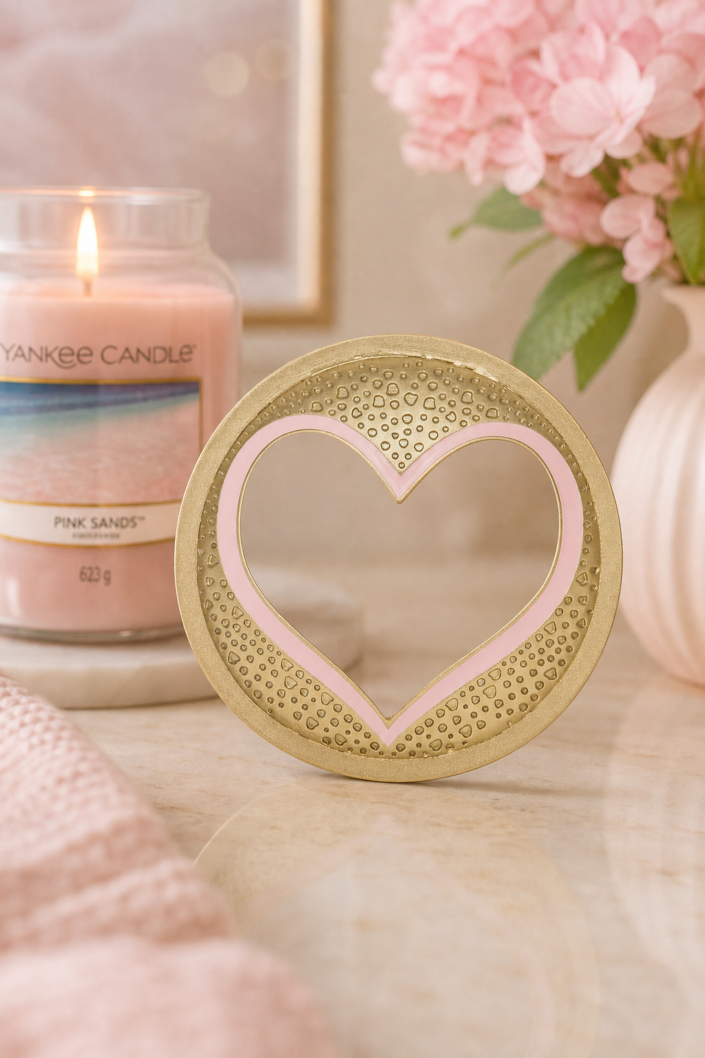 Goldener Illuma-Lid mit rosa Herzrahmen vor brennender Yankee Candle