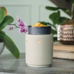 Elektrische Duftlampe mit orangefarbenen Würfeln auf einer Oberfläche neben einer Orchidee