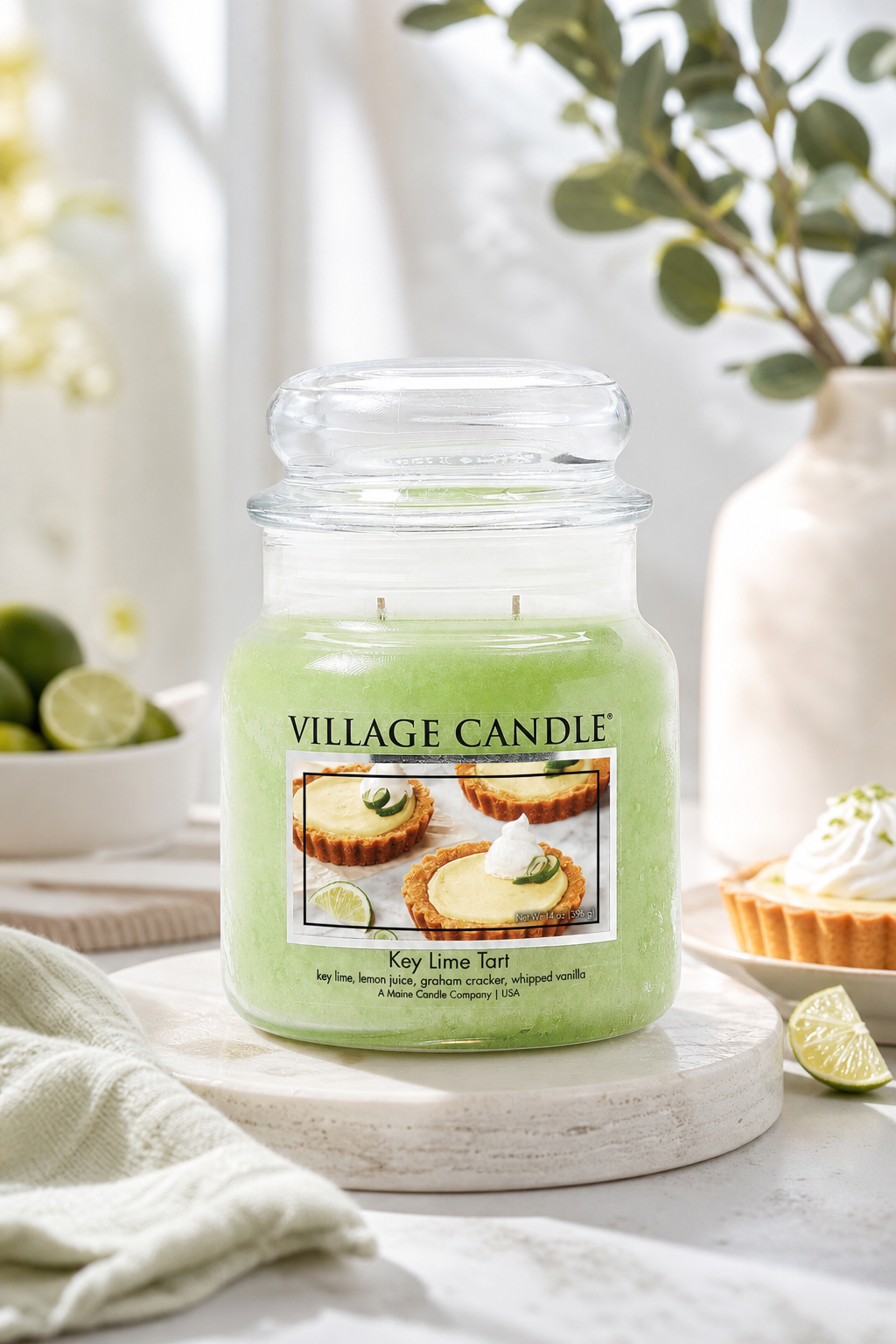 Village Candle Key Lime Tart auf einem Tisch neben Limetten und Törtchen