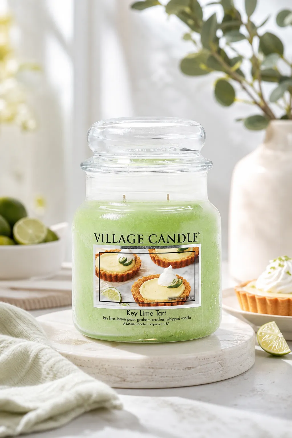 Village Candle Key Lime Tart auf einem Tisch neben Limetten und Törtchen