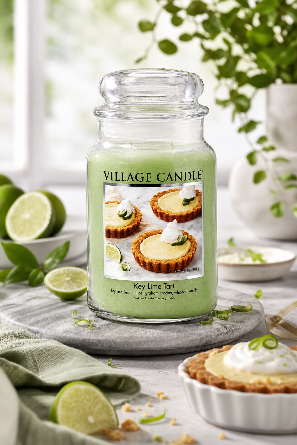 Key Lime Tart Kerze von Village Candle steht neben Limetten und Limettentörtchen