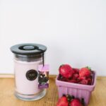 Rosa Kerze im Glas neben einer Schale mit Erdbeeren