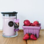 Rosa Kerze im Glas neben Erdbeeren auf einem Holztisch
