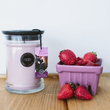 Rosa Kerze im Glas neben Erdbeeren auf einem Holztisch