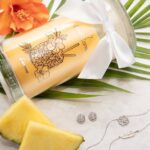 Seitlich liegende Jewel Candle L’Ananas neben Ananasscheiben und Schmuckstücken