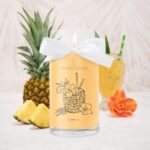 JewelCandle-Kerze mit Schleife vor Ananas, Ananasstücken und Getränk