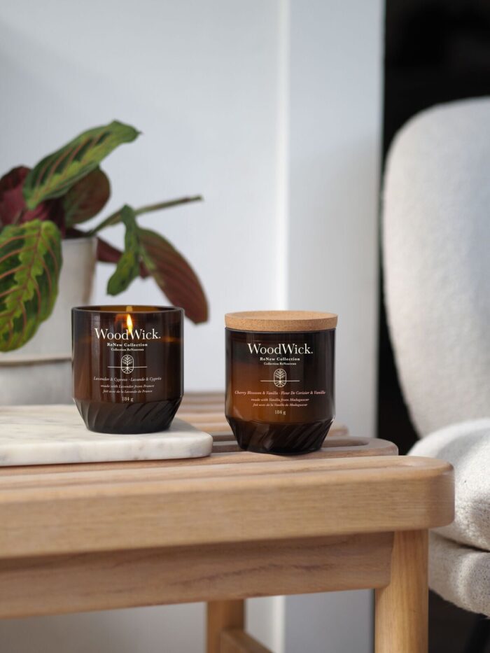 Mehrere WoodWick ReNew Collection Kerzen auf Beistelltischen vor einem Sofa