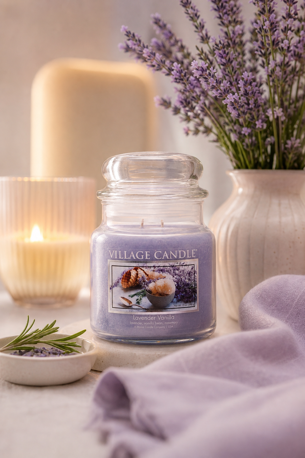 Lavender Vanilla Kerze von Village Candle neben Lavendelstrauß und brennender Kerze