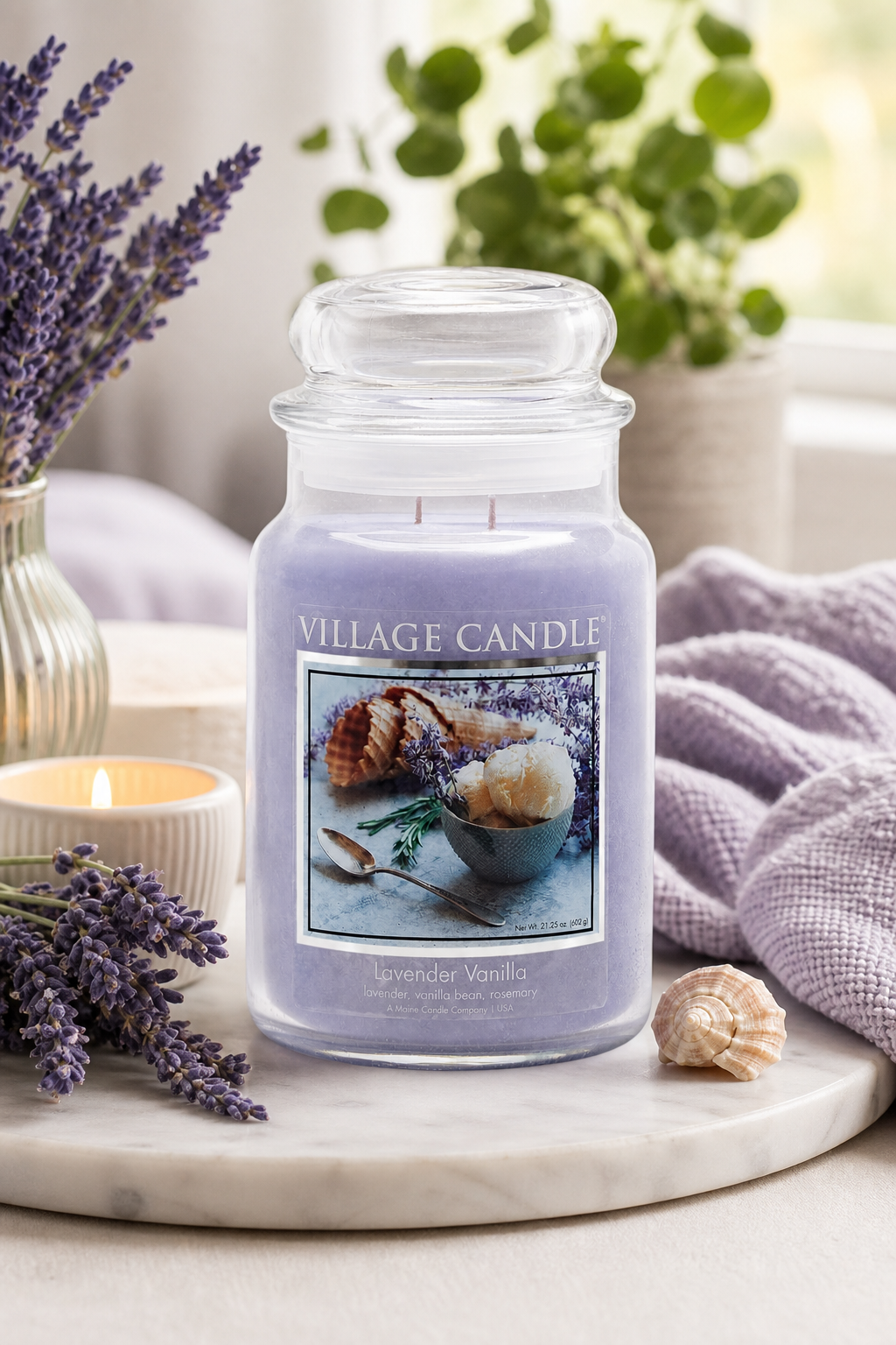 Lavender-Vanille-Kerze auf einer Marmorscheibe neben Lavendel und Textilien
